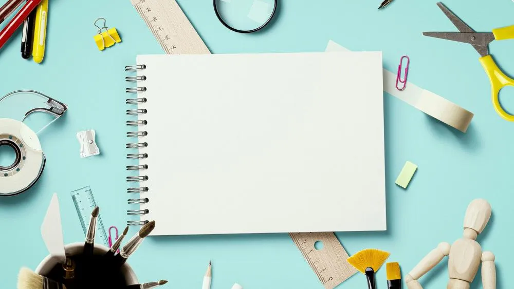 Desktop stationery scene with a blank spiral notebook surrounded by tape, scissors, rulers